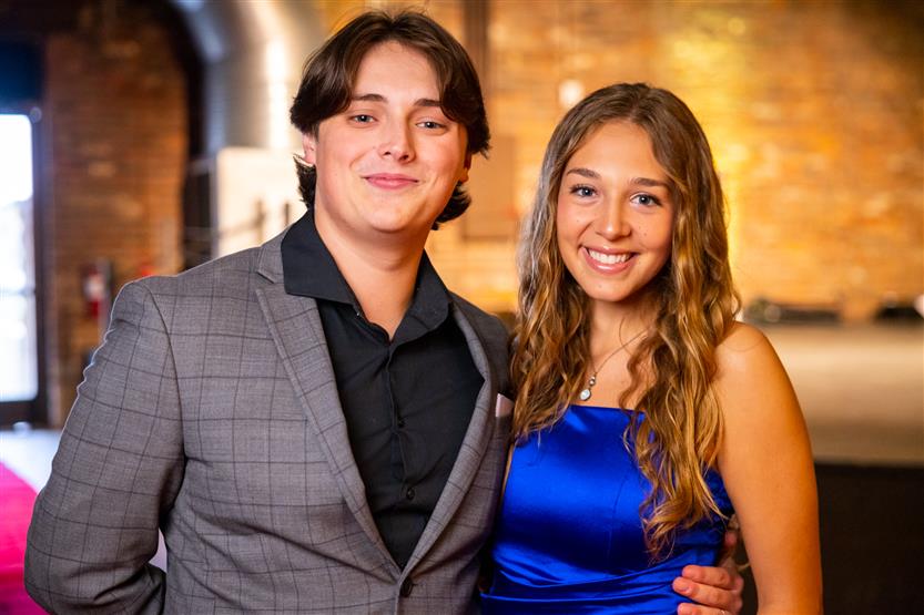 A man wearing a checked grey blazer smiles with a woman wearing blue